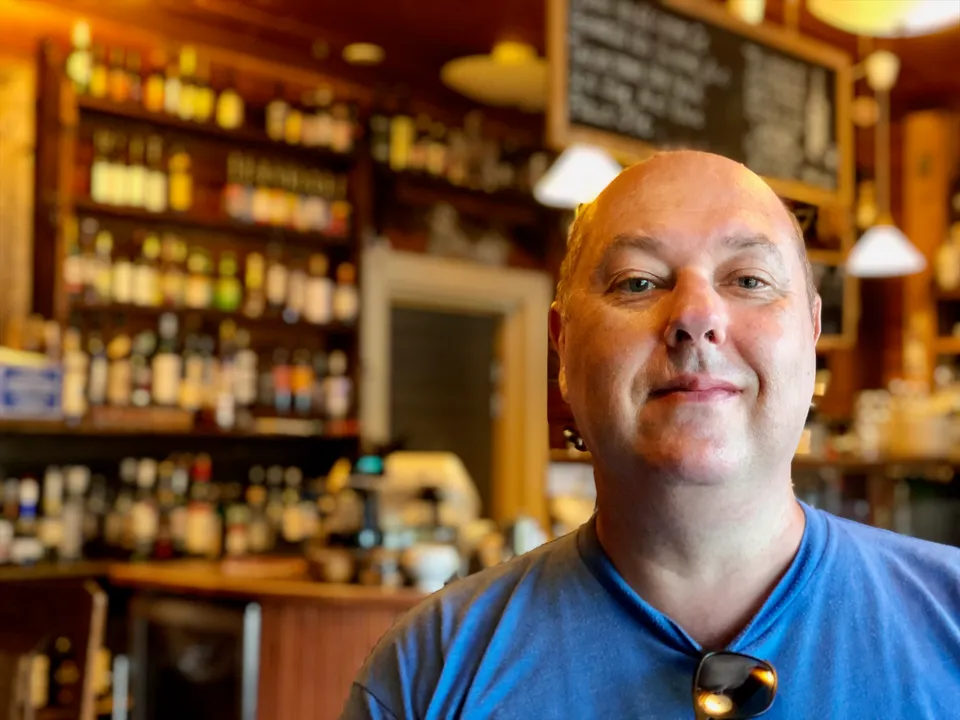 Dave Sag smiling in a blue T-shirt in a warmly lit bar